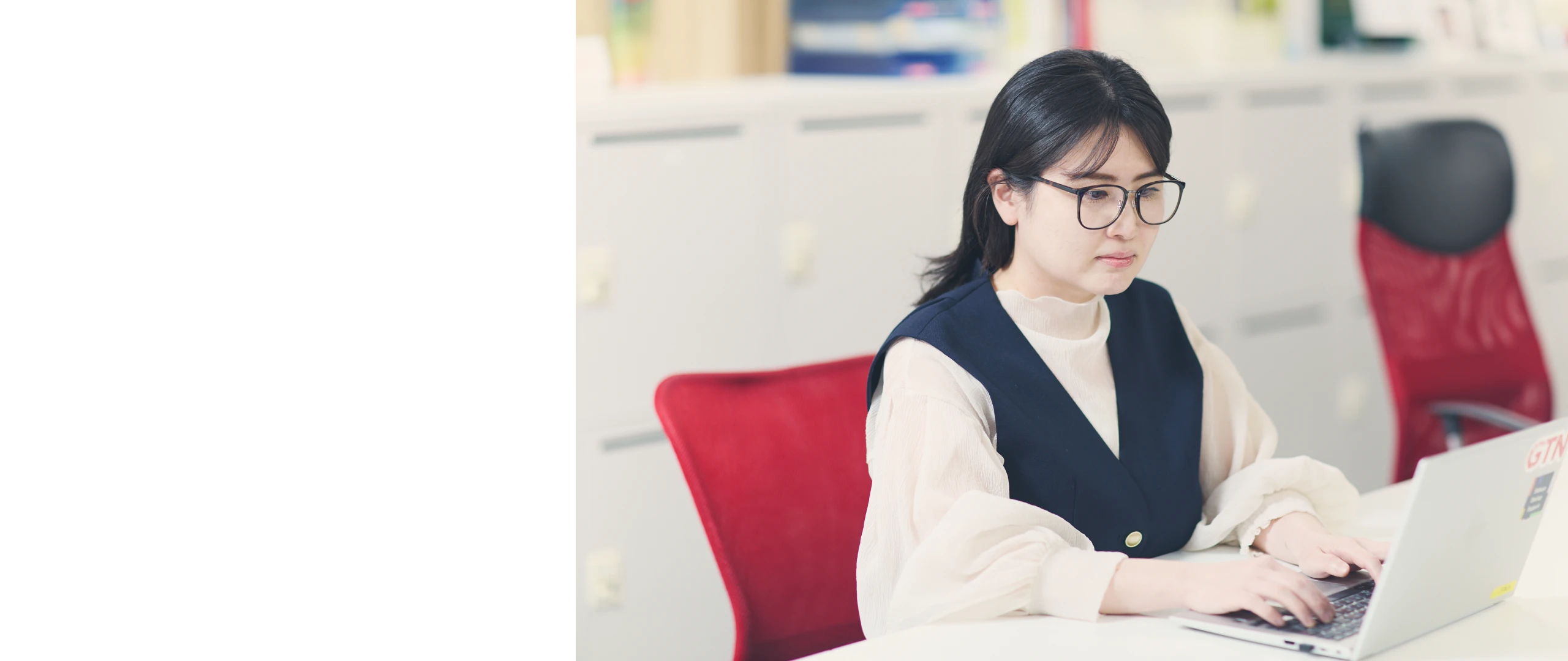 赤いオフィスチェアに座りノートPCで作業する女性社員