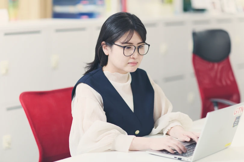 赤いオフィスチェアに座りノートPCで作業する女性社員