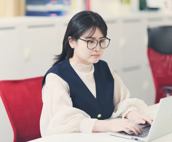 赤いオフィスチェアに座りノートPCで作業する女性社員