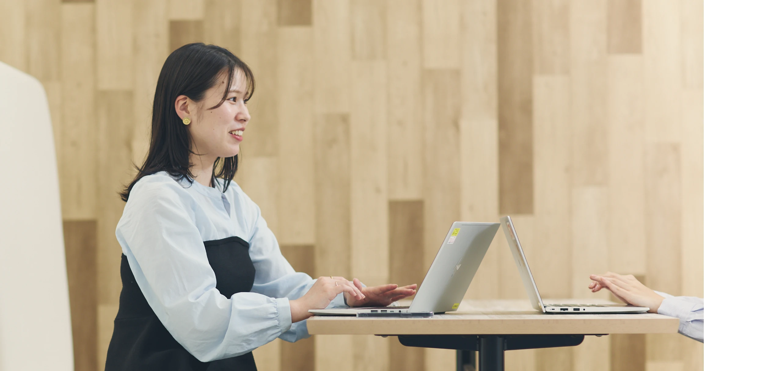ノートPCを使いながら笑顔で同僚と話す女性社員