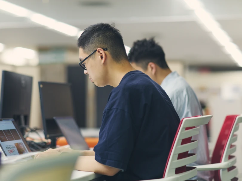 オフィスでモニターに向かって集中して作業する男性社員2人