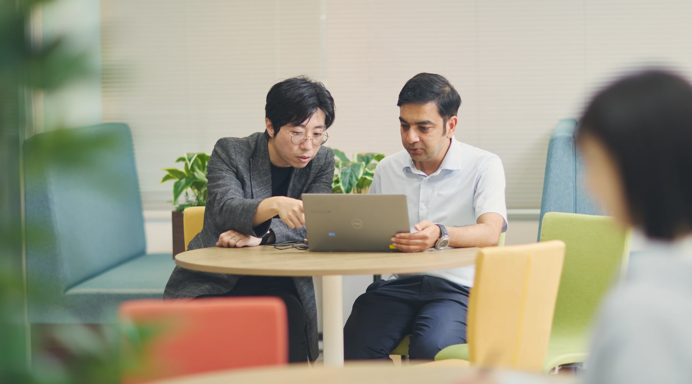 オフィスでノートPCを見ながら打ち合わせをする男性社員2人