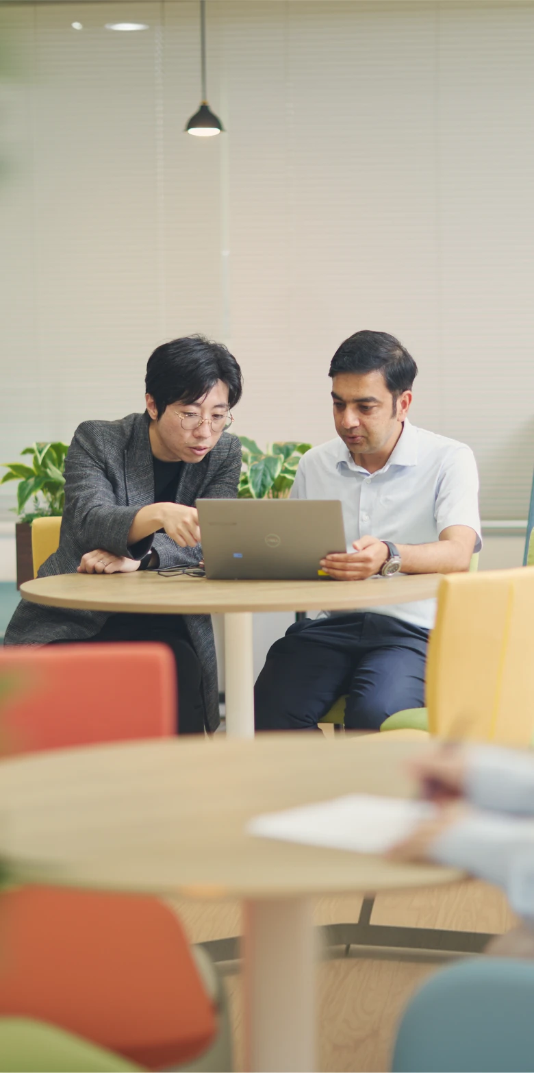 オフィスでノートPCを見ながら打ち合わせをする男性社員2人