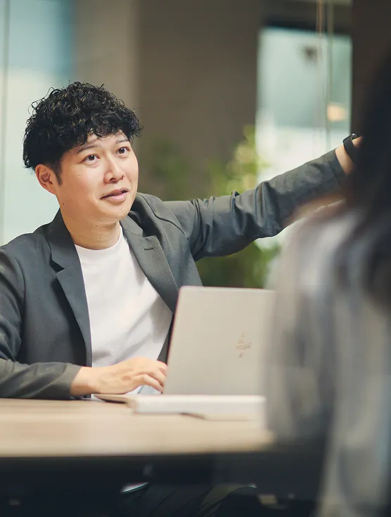 オフィスで同僚に向けて話しながら指を指す男性社員