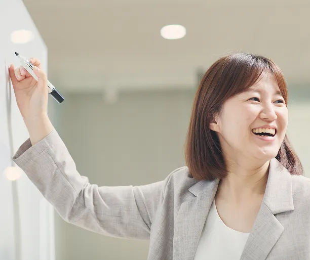ホワイトボードの前でマーカーを持ち笑顔を見せる女性社員