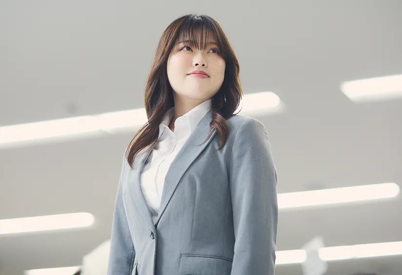 グレーのジャケットを着け前を見上げて微笑む女性社員